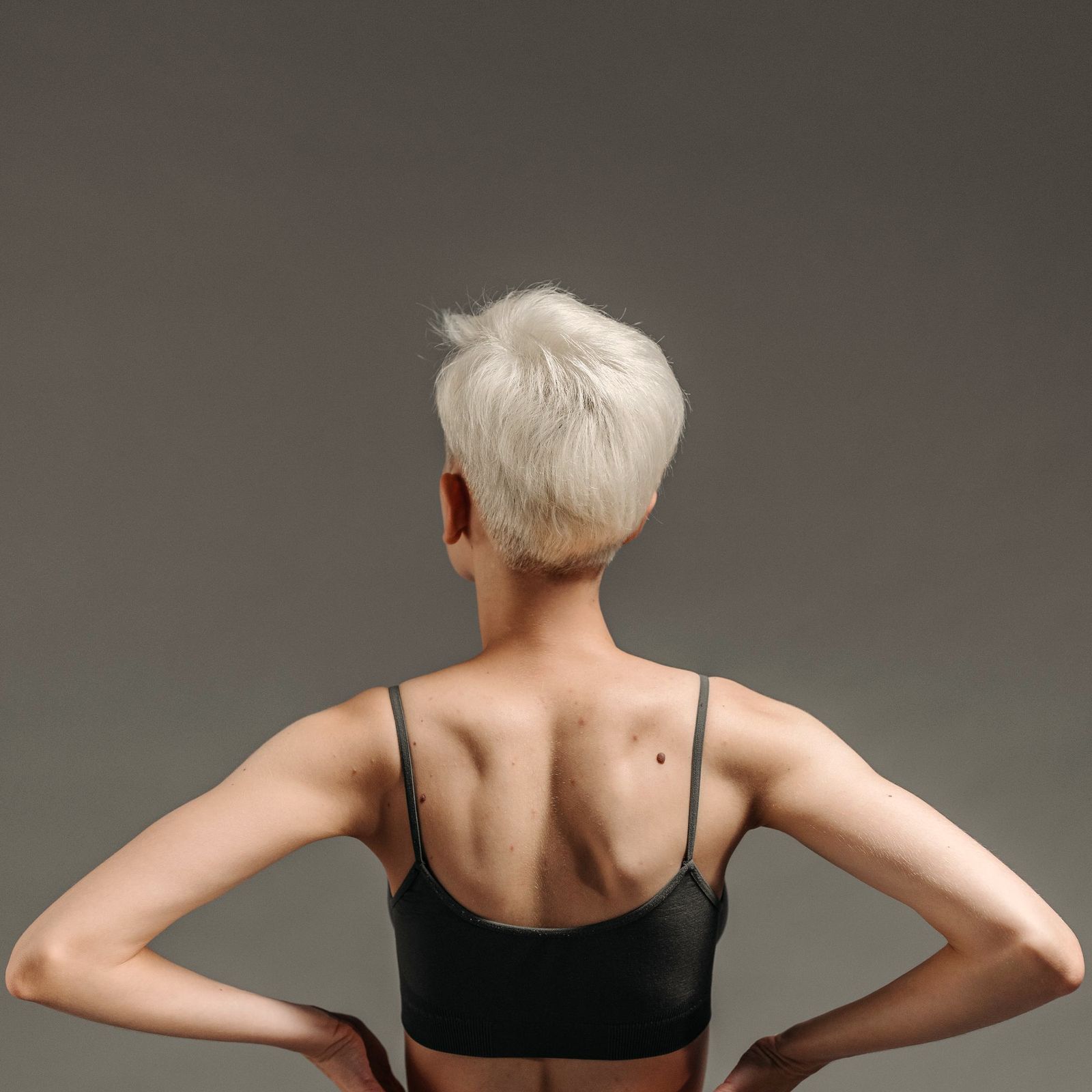 A model with a platinum pixie cut seen from behind in a grey studio