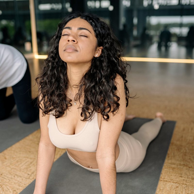 A woman with dark curls in a cream ribbed set in cobra pose on a cork floor