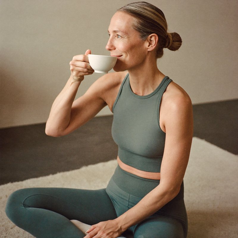 A silver-haired woman in a moonstone set sipping tea cross-legged after practice