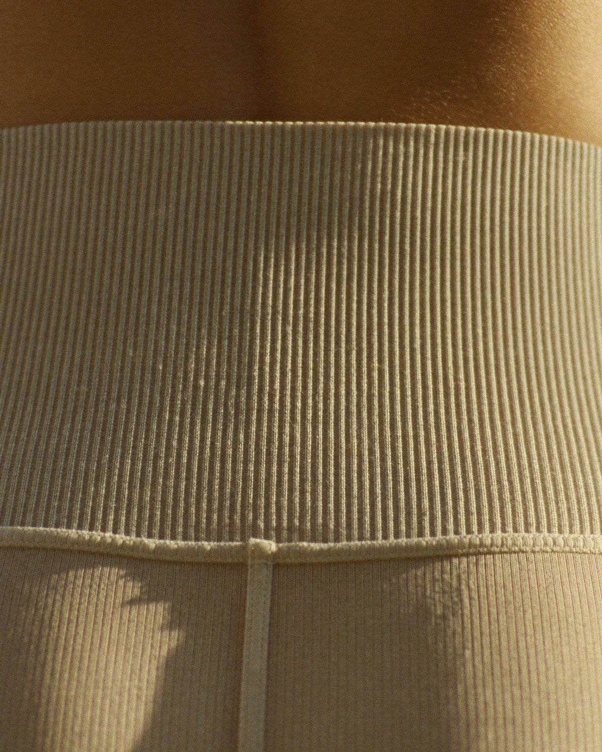 Macro shot of the high-waist legging's ribbed waistband in raking golden light
