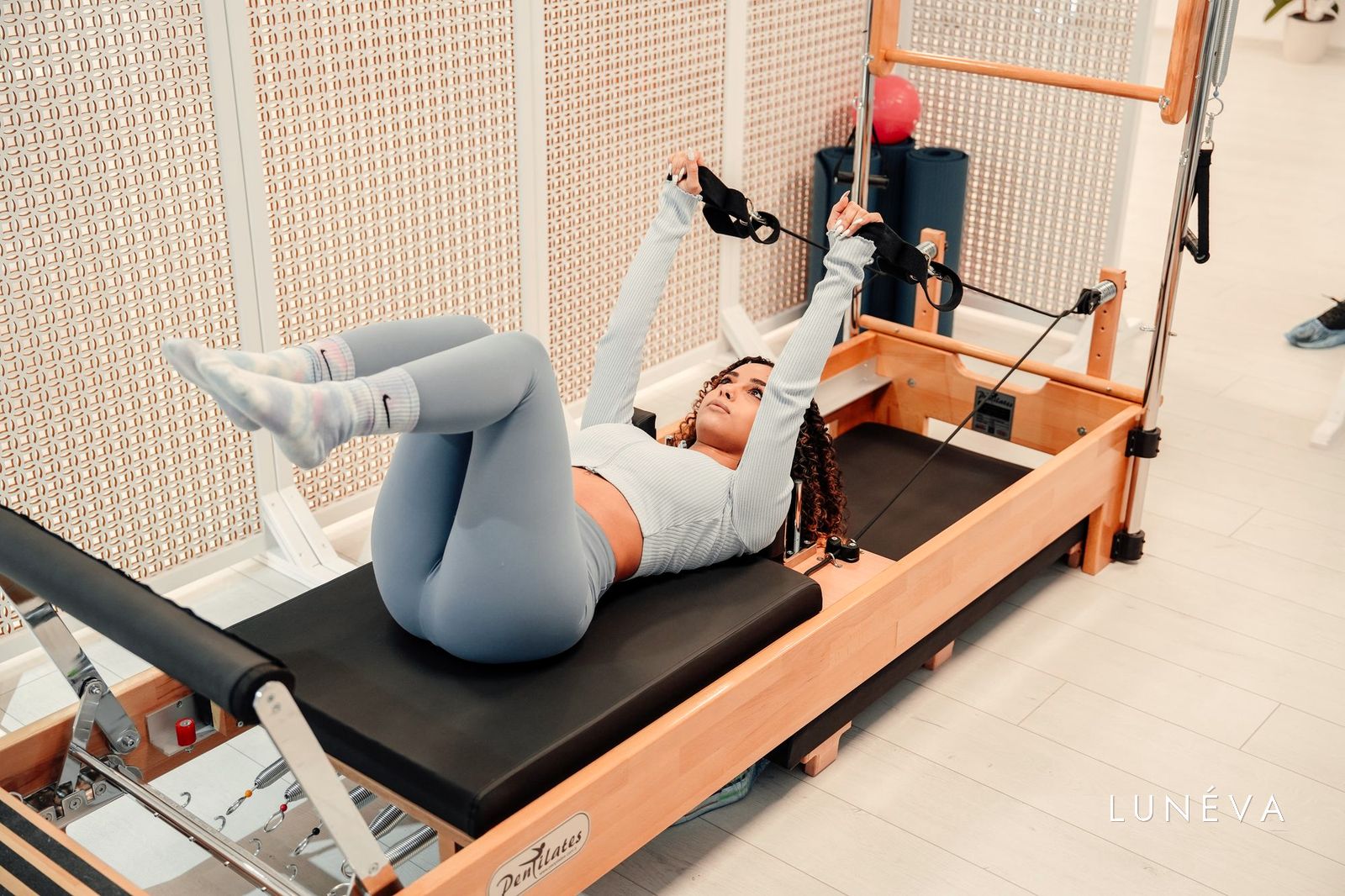 A woman lying on a pilates reformer with a warm wooden frame